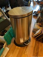 Full view of the oval stainless steel trash can with black base and foot pedal, showing overall condition and size relative to surroundings.