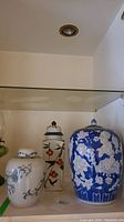 Three ceramic ginger jars of varying sizes and blue, white, and brown colors, placed on a shelf.