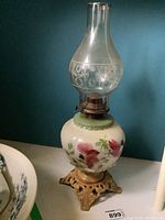 Full view of the oil lamp showing the clear etched glass chimney, floral hand-painted glass body, and ornate metal base