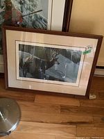 Framed Robert Bateman print leaning against wall showing two deer in snowy forest, brown wood frame and beige mat.