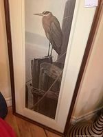 Framed print showing heron perched on wooden posts by water with natural colors and signature visible