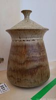 Front view of the lidded stoneware jar showing the tapering cylindrical body with brown and beige glaze.