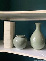 Three ceramic items on shelf: white Rosenthal rectangular vase, light celadon round ginger jar with lid, and light celadon pear-shaped vase