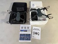 Two collapsible quadrocopter drones shown with their remote controllers, manuals, and cables laid out on a table.