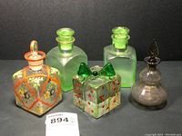 Photo showing the full set of five glass pieces: two green bottles, one gray perfume bottle, one hand-painted jar, and one glass gift paperweight present.
