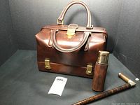 Photo of vintage leather doctor's bag with mini leather-covered glass flask and wooden cane with monogram 'R' handle.