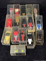 Front and top view of 16 Matchbox Lesney Models of Yesteryear die-cast vintage cars, all in clear plastic display boxes arranged in rows on a black surface.