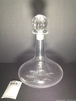 Clear vintage Orrefors crystal decanter with broad base and stopper, shown front and side angles.