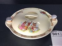 Top view of the bowl with lid on, showing colorful Bunnykins bunny characters and floral design on lid and bunny border on rim