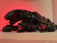 Close-up of the large gloss black ceramic panther figurine showing missing eye gem and part of the wired light inside casting a red glow.