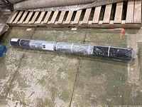 Full view of rolled IKEA area rug in plastic packaging lying on floor.