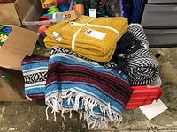 Photo of yellow knit blanket, black and white chevron patterned blanket, and multicolored woven blanket with white fringe in a tote.