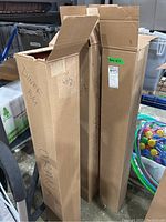 Three tall cardboard boxes containing the corrugated paper rolls, marked with text.