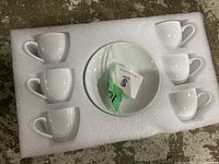 Eight white ceramic cups and one white ceramic bowl arranged in foam padding.