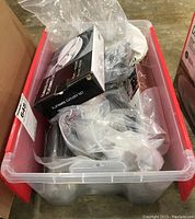 Plastic bin filled with flatware sets and serving utensils, many still in plastic bags.