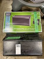 Two metal mailboxes shown, one black used mailbox on floor, one new in box mailbox with green packaging.