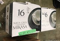 Two cardboard boxes labeled Mikasa Naya Grey 16 piece and 6 piece incomplete sets