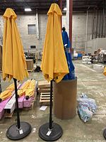 Two yellow patio umbrellas with black poles and round bases standing in an industrial setting.