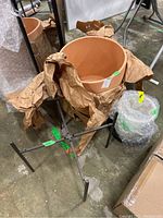 Large terra cotta planter, metal stand and smaller planter partially wrapped in brown paper.