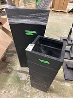 Two black metal square tapered planters placed side by side, one smaller (12x12x26) and one larger (16x16x36)