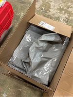 Open cardboard box containing gray plastic bags folded neatly inside.