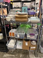 Front view of metal shelving containing stacked white dishes, flattened cardboard boxes, plastic bins with glassware, and cardboard boxes below.