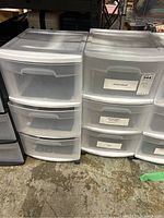 Two white and translucent Sterlite storage bins side by side on a concrete floor, each with three drawers and mounted on black casters. Rightside bin has labels on drawers indicating office supplies.
