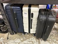 Three hard-shell roller suitcases side by side (dark blue, white, black)