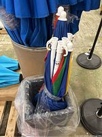 Five folded multi-colored beach umbrellas with white plastic handles held in a container, showing tops and handles.