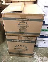Two sealed cardboard boxes from Maher Naturals labeled 'Compostable' containing paper coffee cups and lids.