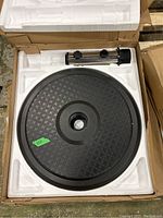 Top-down photo of the black cast iron umbrella base and metal pole holder inside styrofoam packaging in a cardboard box.