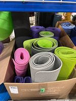 Box containing multiple yoga mats in different colors including pink, green, gray, black, and purple, rolled up and arranged vertically.