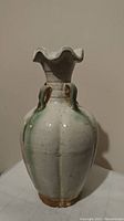 Front view of antique ceramic vase displaying its ruffled top rim, loop handles, and green glaze accents.