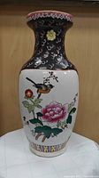 Front view of hand painted Chinese vase showing pink flower and bird on white panel with black background and red/gold rim decorations.