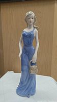 Front view of porcelain figurine of woman in blue dress holding handbag, showing full body and face details.