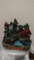 Front view of the indoor desktop relaxation waterfall fountain showing miniature red-roofed house, trees, waterwheel, and water basin with Asian-style characters on front.