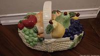 Left side view of ceramic basket showing detailed colorful ceramic fruits and woven basket texture.