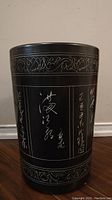 Front side of the black ceramic vase showing white Chinese calligraphy and floral borders on the top and bottom.