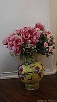 Full view of Chinese yellow porcelain vase with pink and white artificial flower arrangement on wooden floor near wall corner.