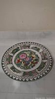 Full view of round ceramic plate showing floral and bird hand painted designs on face and border.