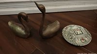 Two copper goose figurines and a decorative plate on wooden floor