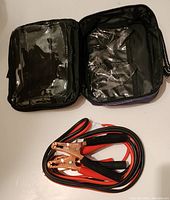 Open black carry case with transparent compartments, and coiled 8-foot red and black booster cables with copper clamps on white surface.