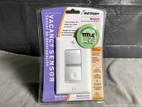 Front view of new Watt Stopper Vacancy Sensor retail packaged, highlighting built-in night light feature and dual language labeling for bedroom and bathroom.