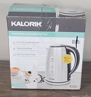 Box of Kalorik Rapid Boil Electric Kettle with front view showing product information and features including 7 cup capacity, 1750 watt power, cordless design, boil dry protection, and faster boiling claim.