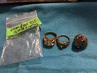 Three rings and empty plastic bag labeled 'sterling 925 gold overlay' on blue cloth