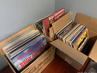 Two cardboard boxes filled with vinyl LP sleeves. Front records visible include Eddy Arnold, Blue Christmas Elvis Presley, Rockin’ with Jerry Lee Lewis.
