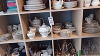 Shelving unit with trays showing stacks of dinner and salad plates, coffee and tea service pieces