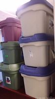 Stacked plastic storage bins in purple, beige, green, and white colors, showing lids and labels.