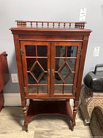 Front elevation view showing double glass doors, brass hardware, spindle gallery top and turned legs.