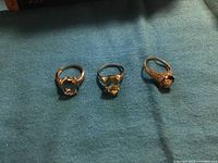 Three rings arranged side by side on blue cloth, showing clear, pale yellow, and blue-purple gemstones